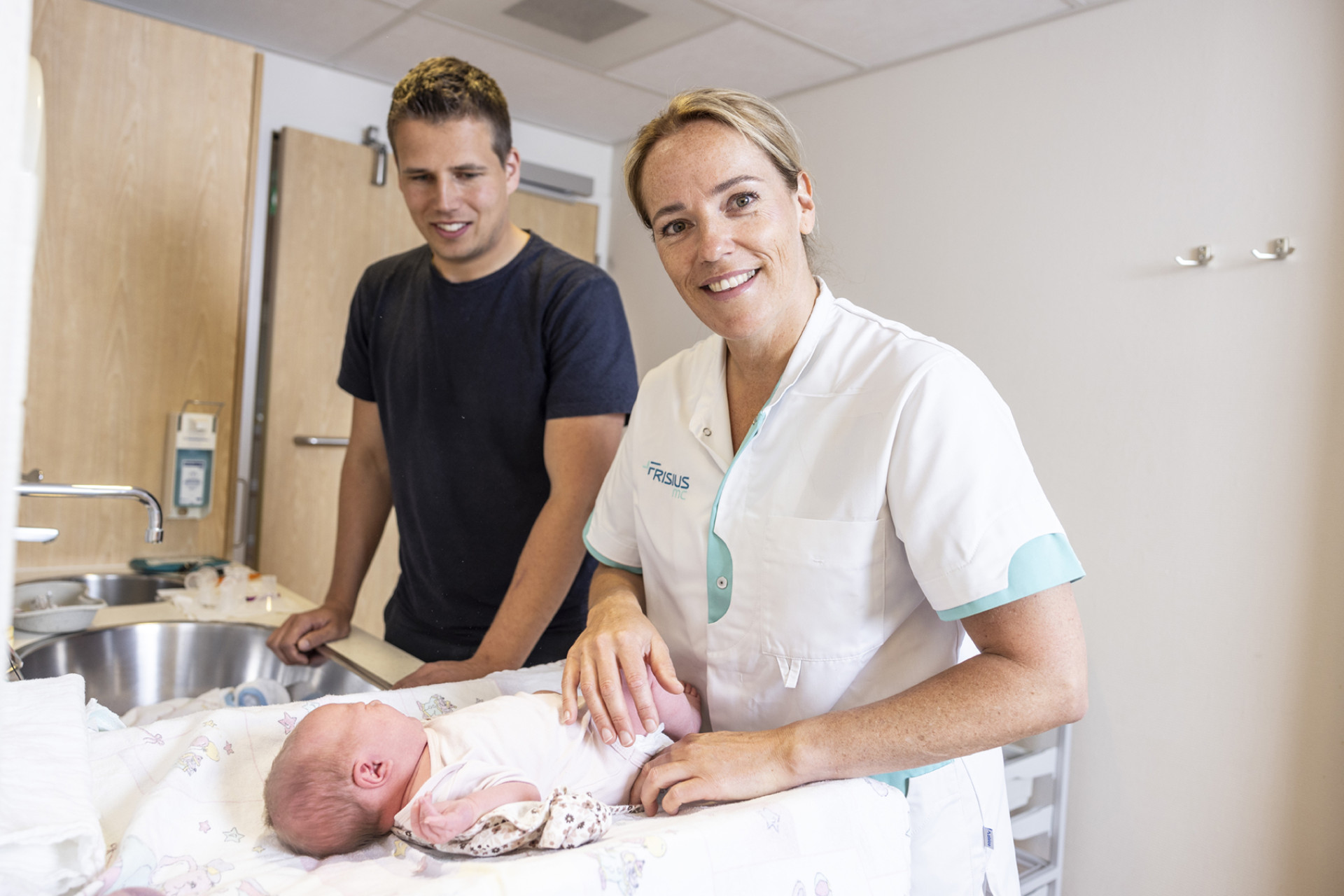 Een verpleegkundige van Frisius MC helpt met de zorg voor een pasgeboren baby, terwijl een man toekijkt.